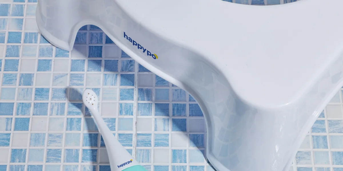 A HappyPo bottle lying on blue mosaic tiles beside a white step stool